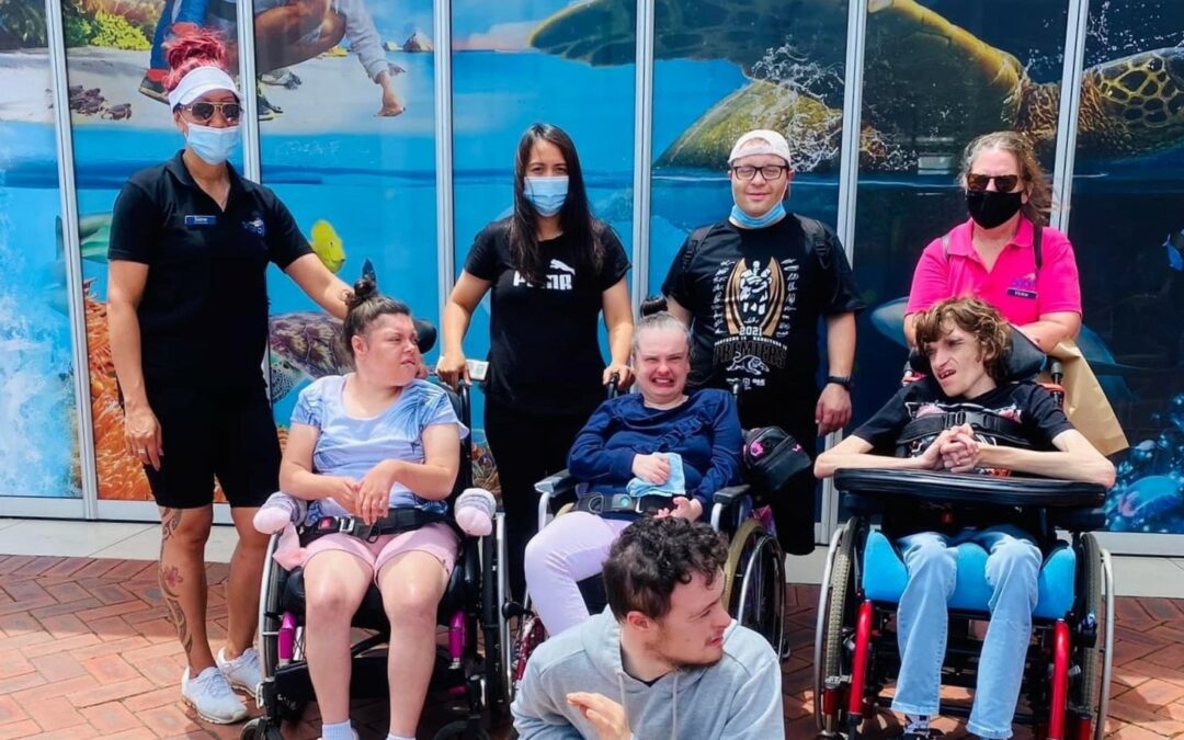 Afford clients and lifestyle assistants are outside the Sydney SEA LIFE aquarium. Three clients are in wheelchairs and everyone is smiling or wearing a face mask.