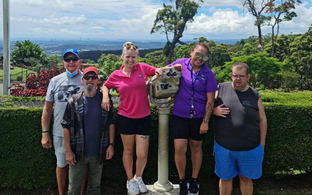 Three male clients standing with two female Afford lifestyle assistants standing alongside a telescope. In the background you can see greenery and a panoramic view of the city skyline.