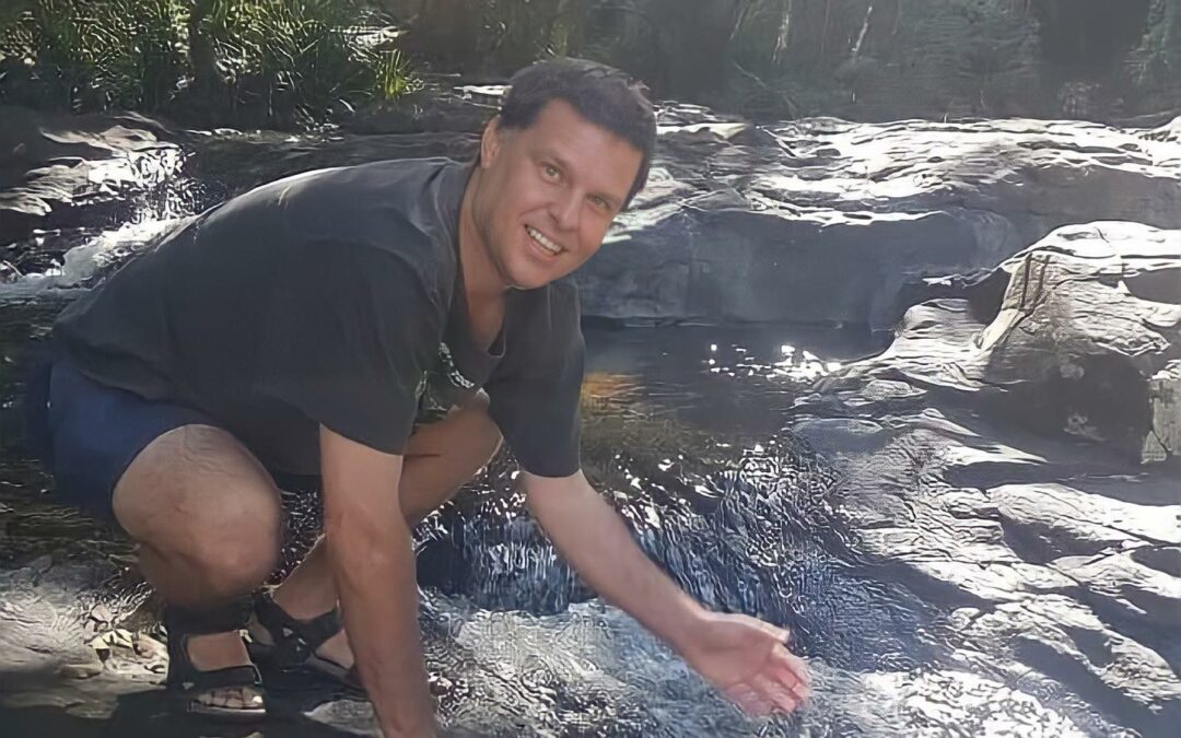 Photo of our client jamie running his hand through the water in a waterfall