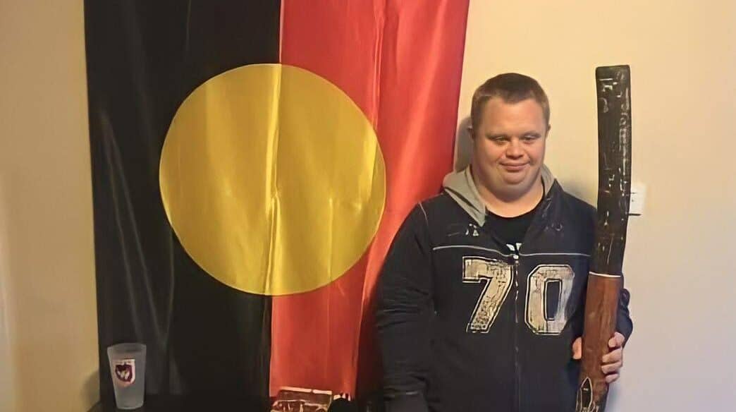 Our client Brys standing with his Indigenous flag and didgeridoo