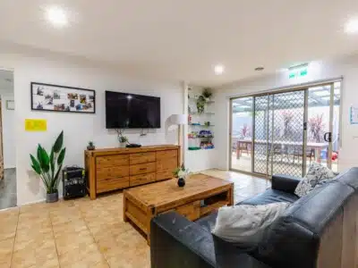 Living room with a black sofa, wooden coffee table and television cabinet. There is a television and shelving on the wall.