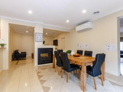 Open plan living and dining area with a fireplace. There is a large wooden dining table with black chairs.