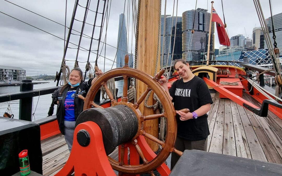 Two clients from Afford's Belmore Community Centre holding the wheel of the Eneadvour ship.