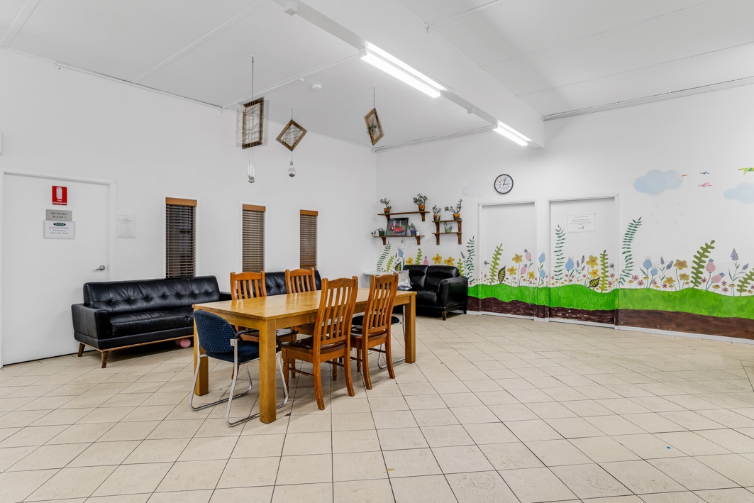 Large open area with a wooden dining table and black sofas.