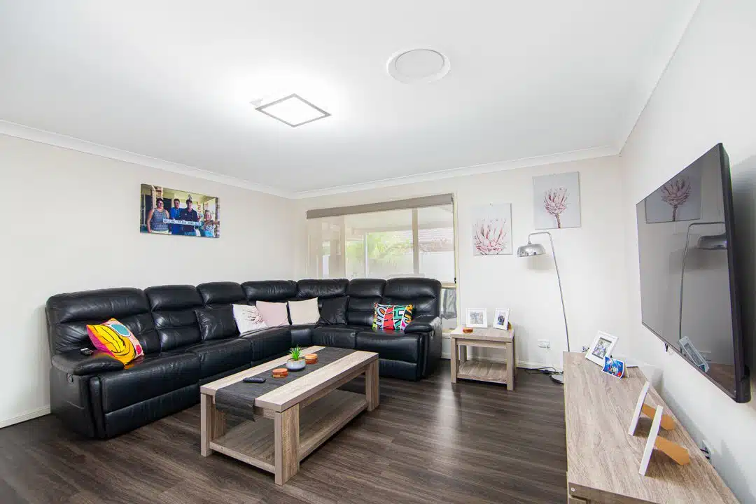 Living room with black leather sofa, wooden coffee table and television stand with a large television.