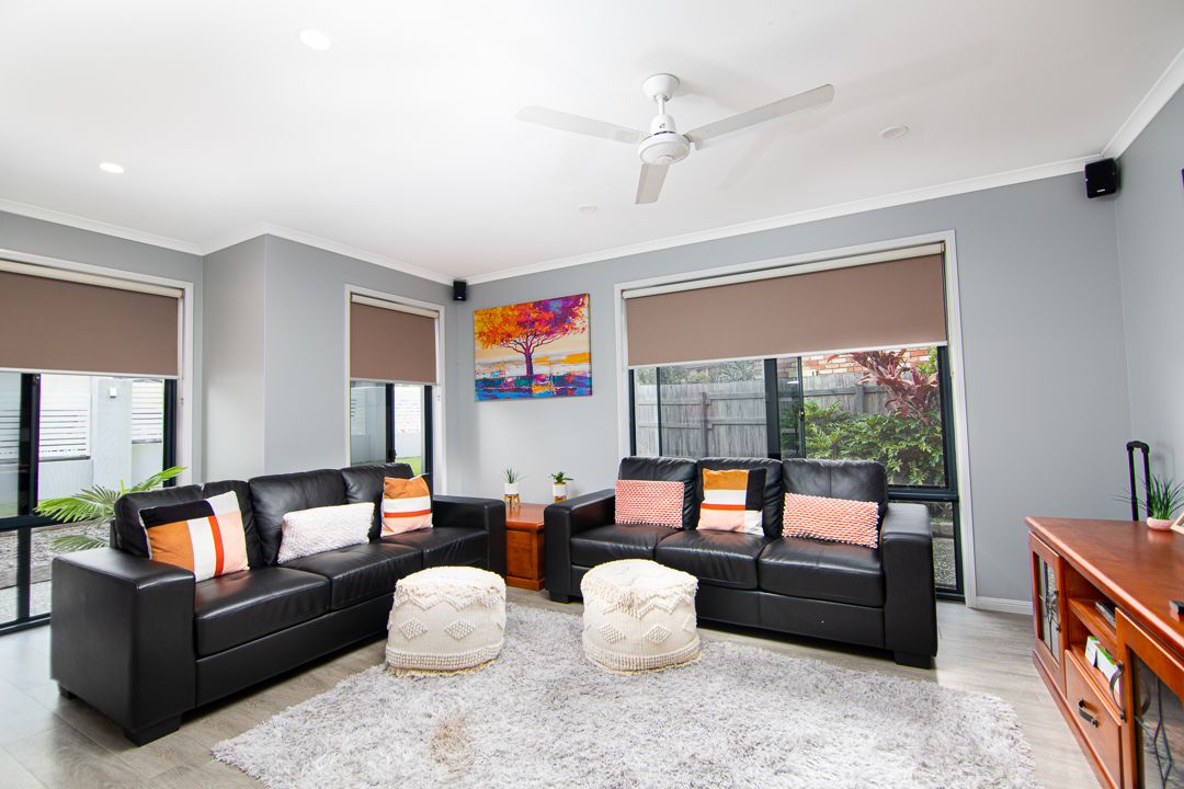 Large living room with two black sofas, a grey rug and three large windows.