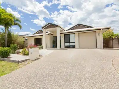 Large SIL house with driveway and grassed front garden with palm trees.