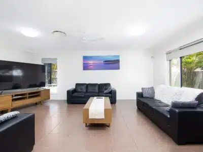 Living room with three black leather sofas, wooden coffee table and a large television.