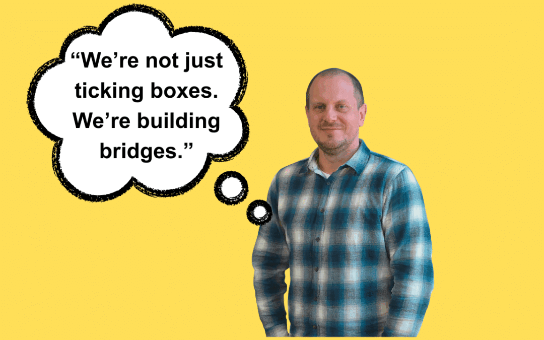 A man wearing a blue checked shirt looks directly at the camera. The words 'We're not just ticking boxes. We're building bridges' appear in a speech bubble next to him.