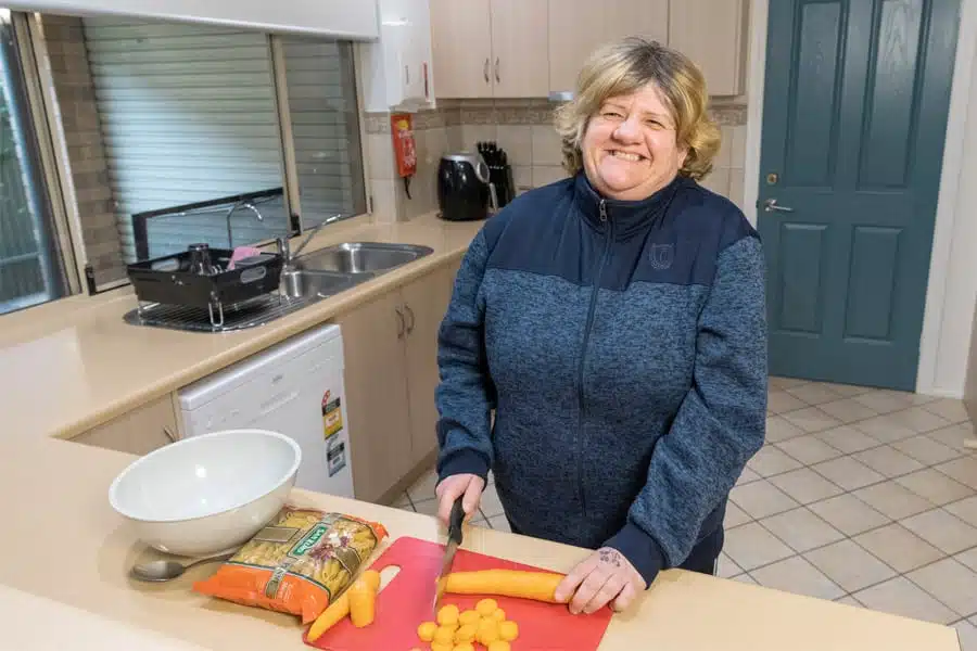 SIL client smiling and cutting vegetables in her kitchen at home.