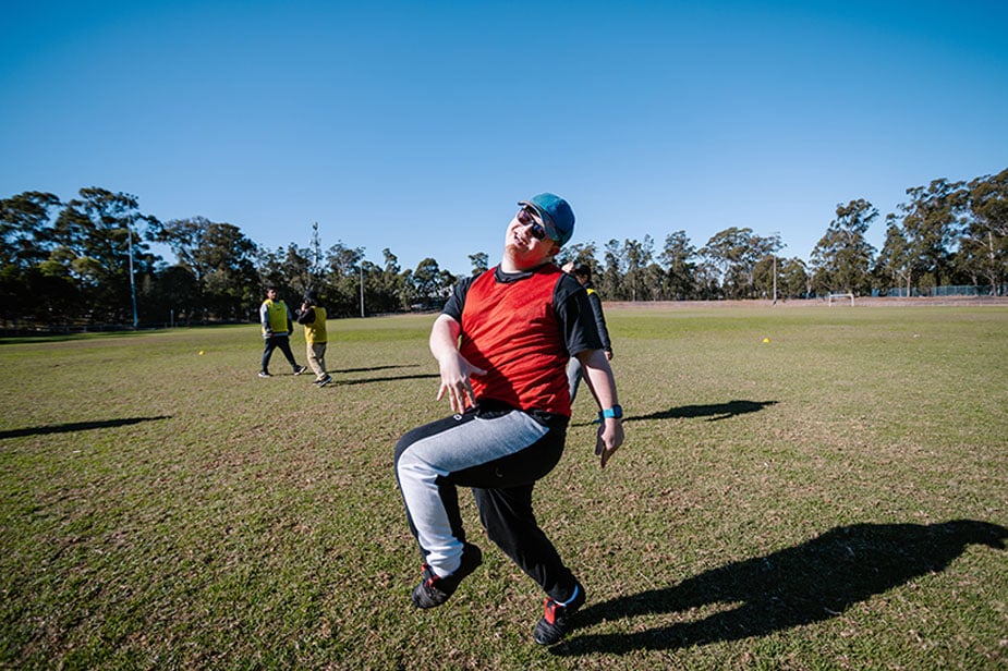 Young man in an Afford hat skipping outside in a park