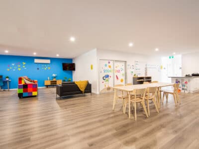 Open plan community hub featuring a dining area, lounge area, computer station and kitchen.