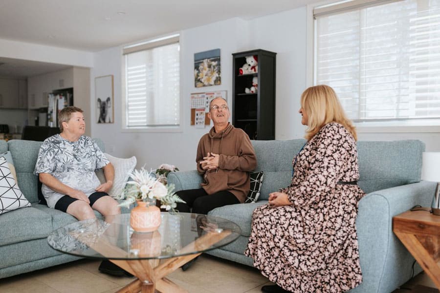 three people sitting on sofas in a living room talking to each other