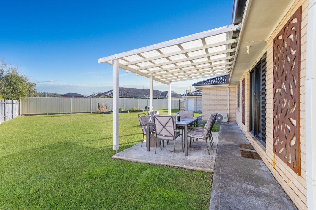 Large grassed garden with an undercover dining area featuring a large table and chairs.
