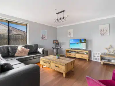 Living room with a large black sofa, pink armchair, wooden coffee table and side tables and a television.