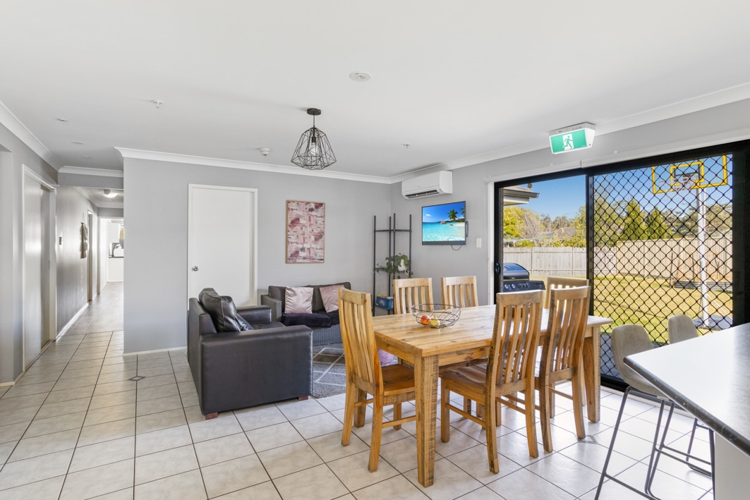 Large open plan living and dining area featuring black leather sofas, wall mounted television and a wooden dining table and chairs.